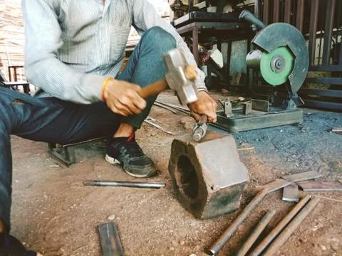Worker beating or hit a iron piece to give a shape in iron workshop with hamm Stock Photos