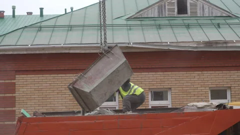 Worker in bed of dump truck assists with loading of bin Stock Footage 311108743
