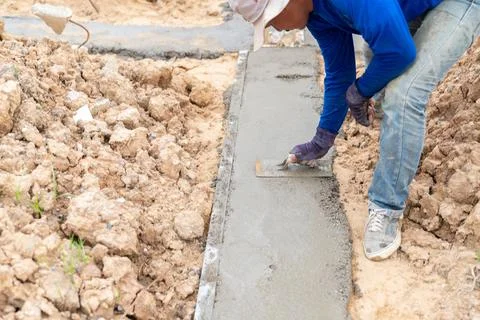The worker is bending down, using a trowel to smooth the surface of the lea.. Stock Photos
