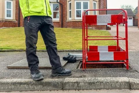 Worker beside open telecoms chamber and barrier on residential street Stock Photos