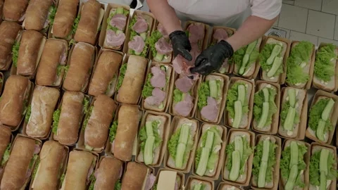 Worker in black gloves assembles sandwiches with lettuce, ham, and cucumbers in Stock Footage 340172437