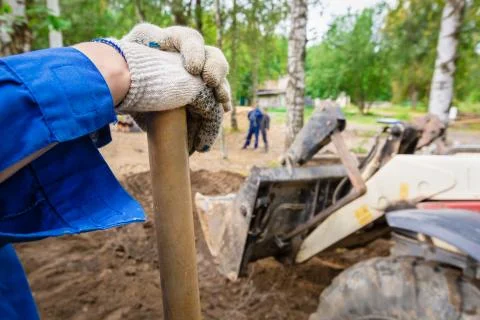 Worker in the blue boilersuit and work gloves with shovel is on the construction Stock Photos