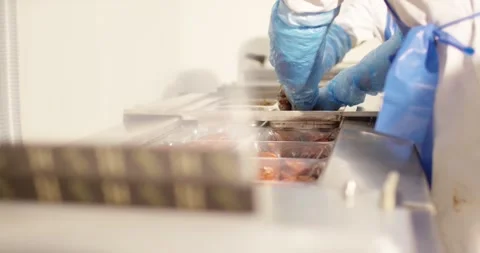 Worker with blue gloves places red sausage products into plastic trays on a Stock Footage 339981917