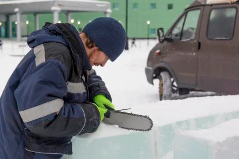 A worker in a blue jacket sharpens a chainsaw chain. 스톡 사진