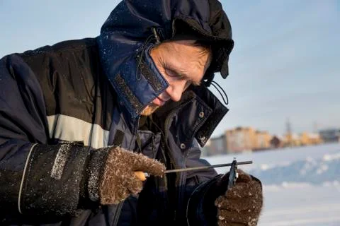 A worker in a blue jacket sharpens a chainsaw chain. 스톡 사진