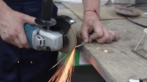 Worker in blue uniform cuts off a metal rod with a grinder Stock Footage 134201324
