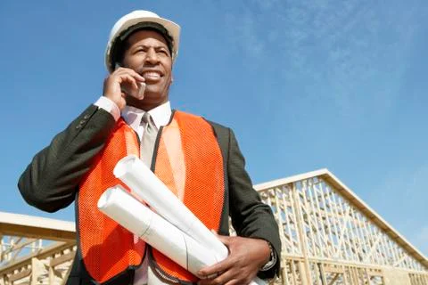 Worker With Blueprints Using Cell Phone At Construction Site Stock Photos