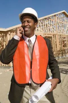 Worker With Blueprints Using Cell Phone At Construction Site Stock Photos