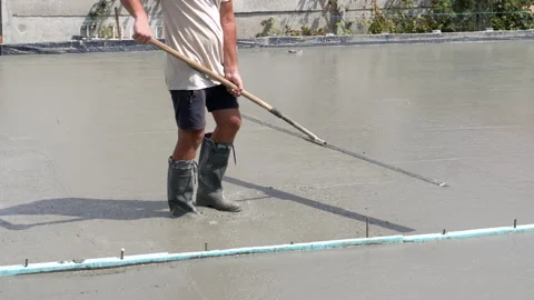 A worker in boots with a hand tool smoothes and levels fresh liquid concrete Stock Footage 309121265