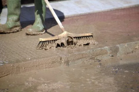 A worker brushes mud off a sidewalk during floods. Foto stock