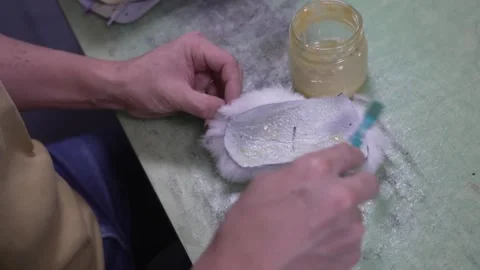 Worker brushing adhesive onto a white padding lining piece for a baseball glove Stock Footage 340156041