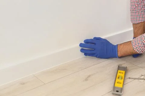 Worker with bubble level installing beautiful plinth on wall in stylish room, Foto stock