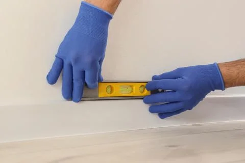 Worker with bubble level installing beautiful plinth on wall in stylish room, Foto stock