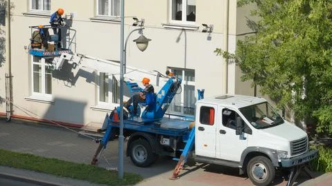 A worker in the bucket of a crane is installing lighting on the facade of the Stock Photos