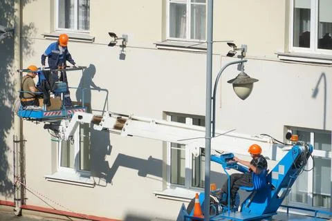 A worker in the bucket of a crane is installing lighting on the facade of the Stock Photos