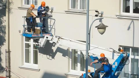 A worker in the bucket of a crane is installing lighting on the facade of the Stock Photos