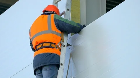 Worker, builder in orange a uniform and hard hat on the construction site Stock Footage 98322190