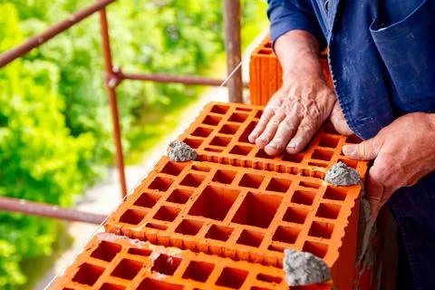 Worker is building wall with red blocks and mortar Stock Photos