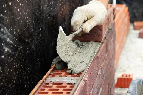 A worker builds a brick wall. Applying cement to brick. Hands in gloves and Stock Photos
