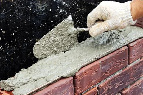 A worker builds a brick wall. Applying cement to brick. Hands in gloves and Stock Photos