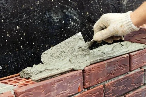 A worker builds a brick wall. Applying cement to brick. Hands in gloves and Stock Photos