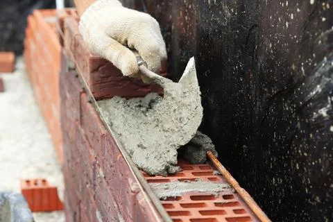 A worker builds a brick wall. Applying cement to brick. Hands in gloves and Stock Photos