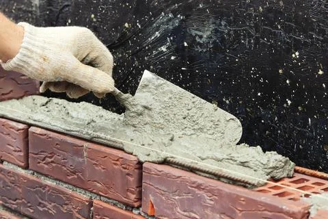 A worker builds a brick wall. Applying cement to brick. Hands in gloves and Stock Photos
