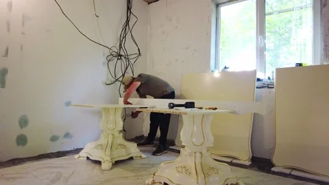 Worker builds table in a room with white walls and hanging wires Stock Footage 340357282