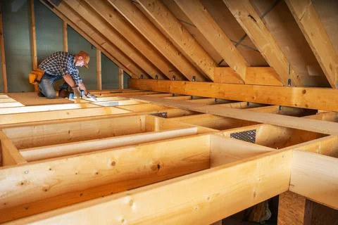 Worker builds wooden framework in attic during daytime Фото