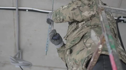 Worker in camouflage jacket measures metal frame on ceiling Видео 313829079