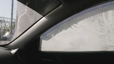 Worker in car washing shop throwing soap on car window. View from inside the car Видео 131132538