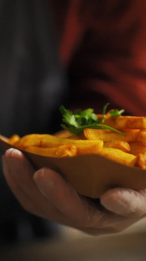 Worker carefully adds fresh herbs to fries in a busy kitchen setting showcas Stock Footage 331740091