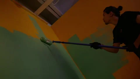 Worker carefully dips roller into wall coat and paints wall Stock Footage 308930156