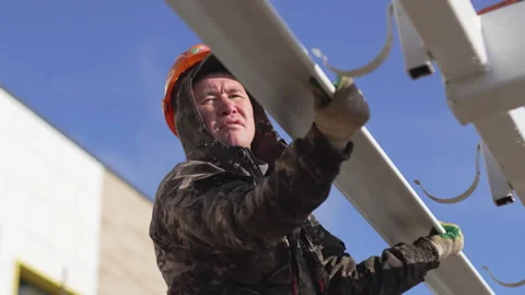 Worker carefully secures shiny metal gutter on large hooks Stock Footage 310243958