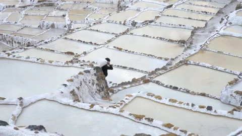 Worker carrying heavy bag through salt pods at Salinas de Maras Stockbeeldmateriaal 202380385