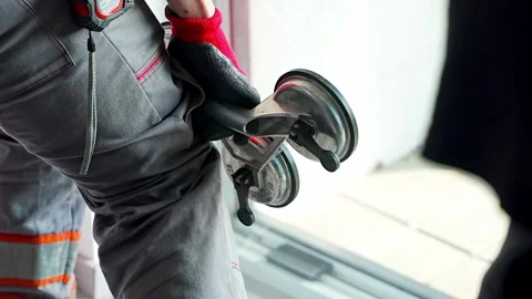 Worker carrying window glass panel using suction cup lifter during installation Stockbeeldmateriaal 344519600
