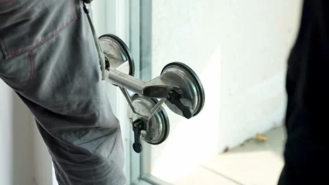 Worker carrying window glass panel using suction cup lifter during installation Stockbeeldmateriaal 344519614
