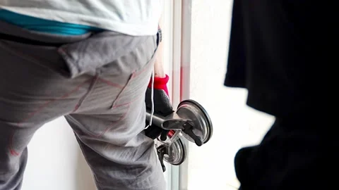 Worker carrying window glass panel using suction cup lifter during installation Stockbeeldmateriaal 344519676