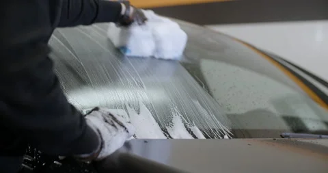 Worker at the carwash cleans vehicle's front window by sponde and foam, 4k 60p Stock Footage 172430737