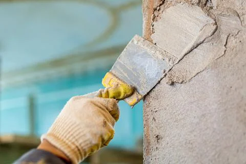 Worker is cementing by the putty knife the wall in room that is under Stock Photos