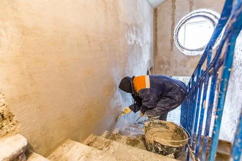 Worker is cementing by the putty knife the wall in room that is under Stock Photos