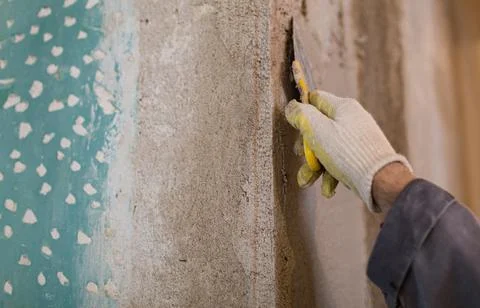 Worker is cementing by the putty knife the wall in room that is under Stock Photos