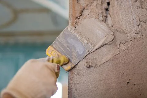 Worker is cementing by the putty knife the wall in room that is under Stock Photos
