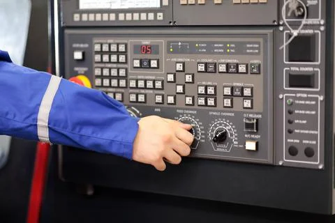 Worker changes feed override of CNC lathe machine Stock Photos