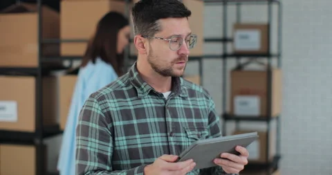 Worker checking inventory, writing notes on tablet. A man works in a warehouse Stock Footage 228675476