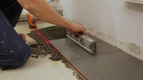 Worker checking level laying tiles on the floor Stockbeeldmateriaal 128415007