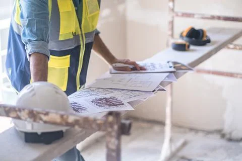 Worker checking renovation project papers lying on construction equipment Stock Photos