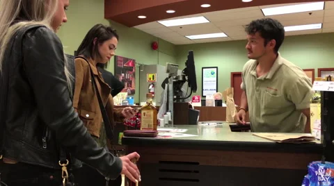 Worker checking young lady ID while her paying wine inside BC liquor store Stock Footage 62977706