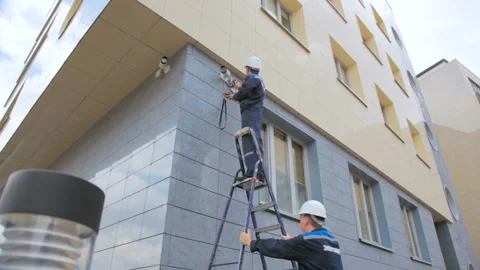 Worker checks CCTV camera operation and colleague holds ladder Stock Footage 91114767