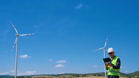 Worker checks data near wind turbines on a sunny day. A worker stands with a Stock Footage 342737410